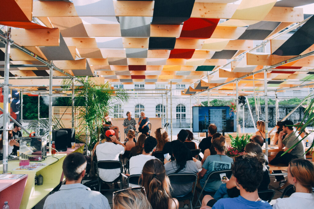 People gathered under a colourful canopy stage on campus
